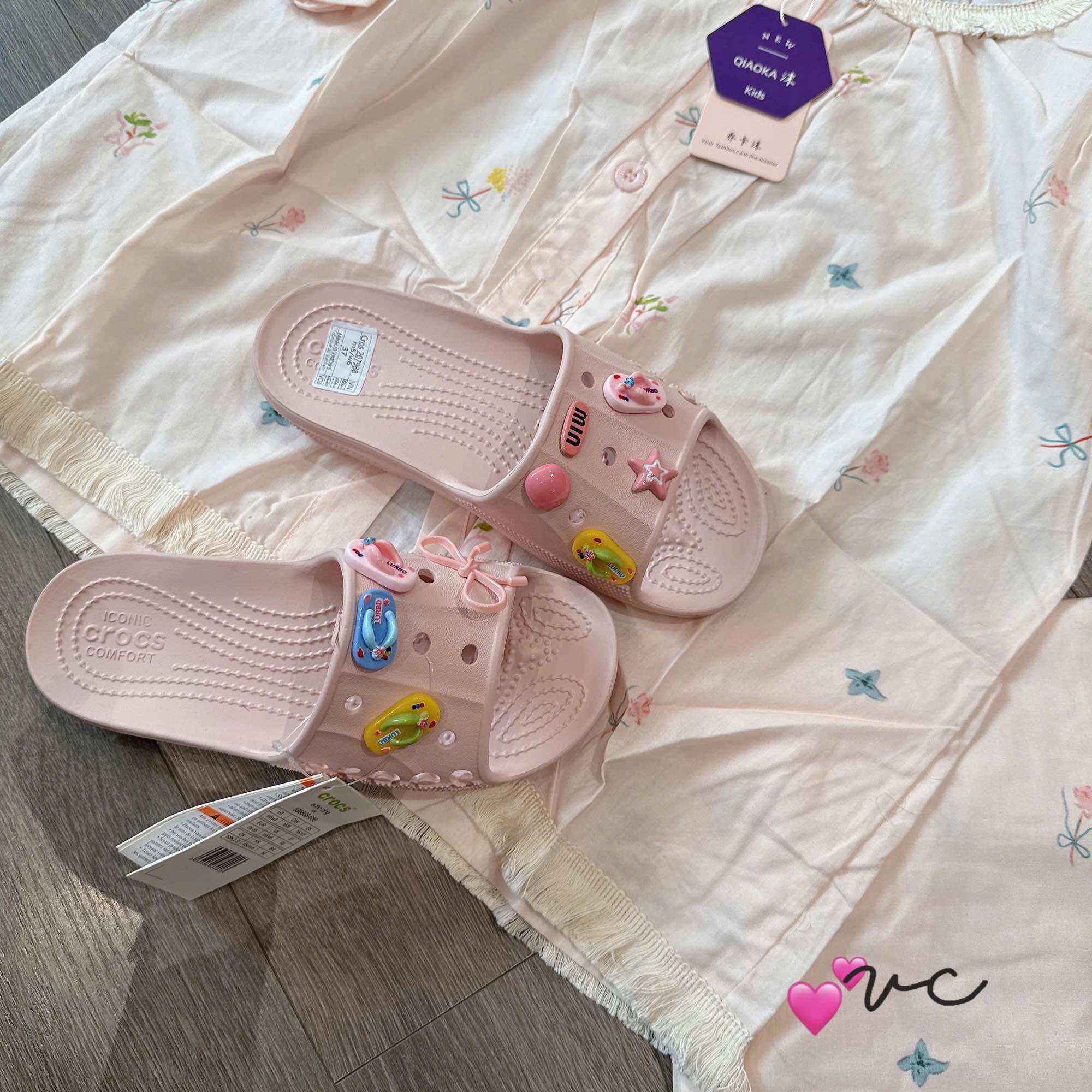 Giày xỏ Crocs màu hồng với các phụ kiện trang trí hình ngôi sao và trái tim, phù hợp cho mùa hè.