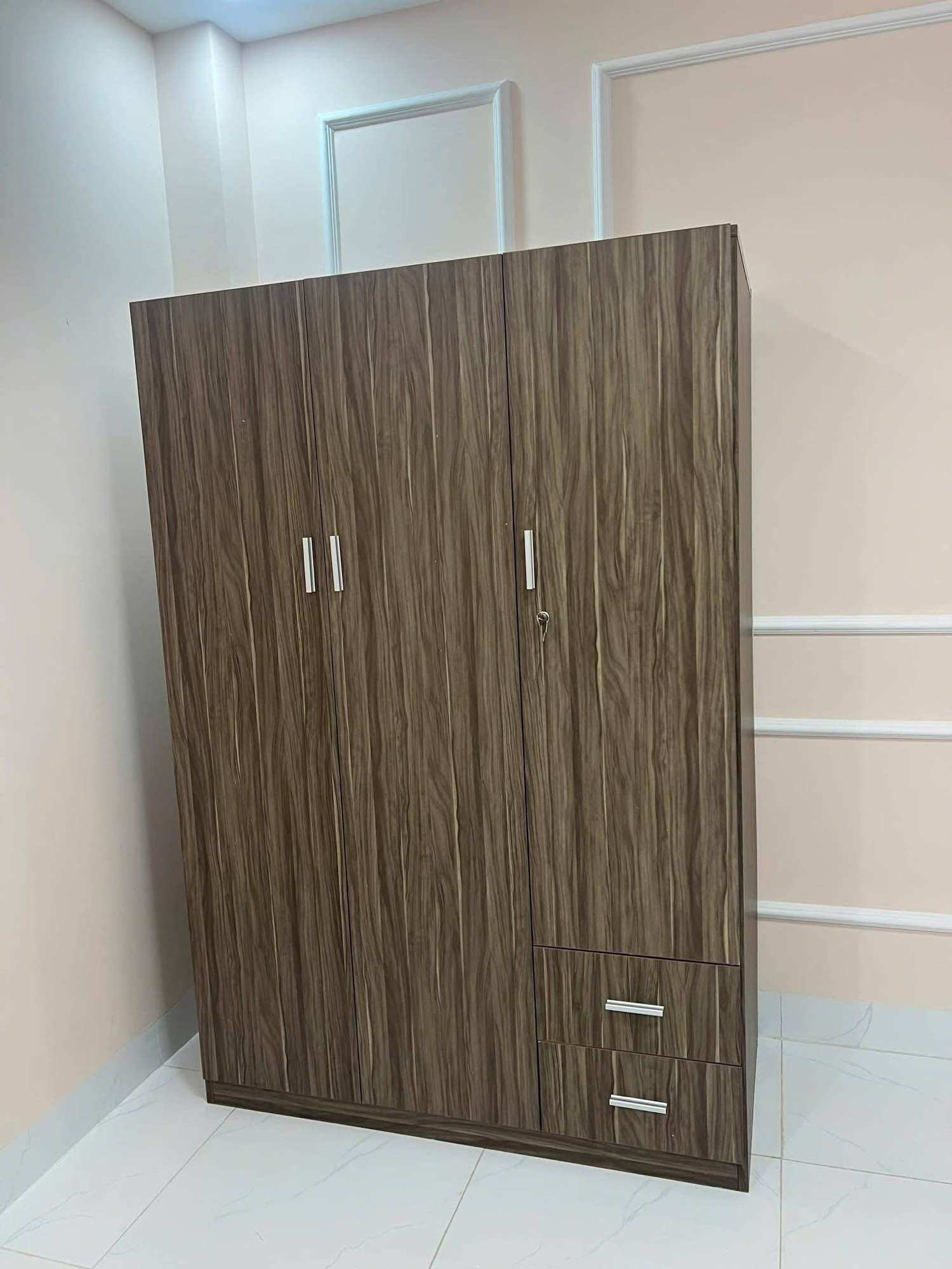Tủ quần áo gỗ màu nâu với vân gỗ tự nhiên, ba cánh cửa và hai ngăn kéo nhỏ ở dưới, phù hợp cho phòng ngủ.